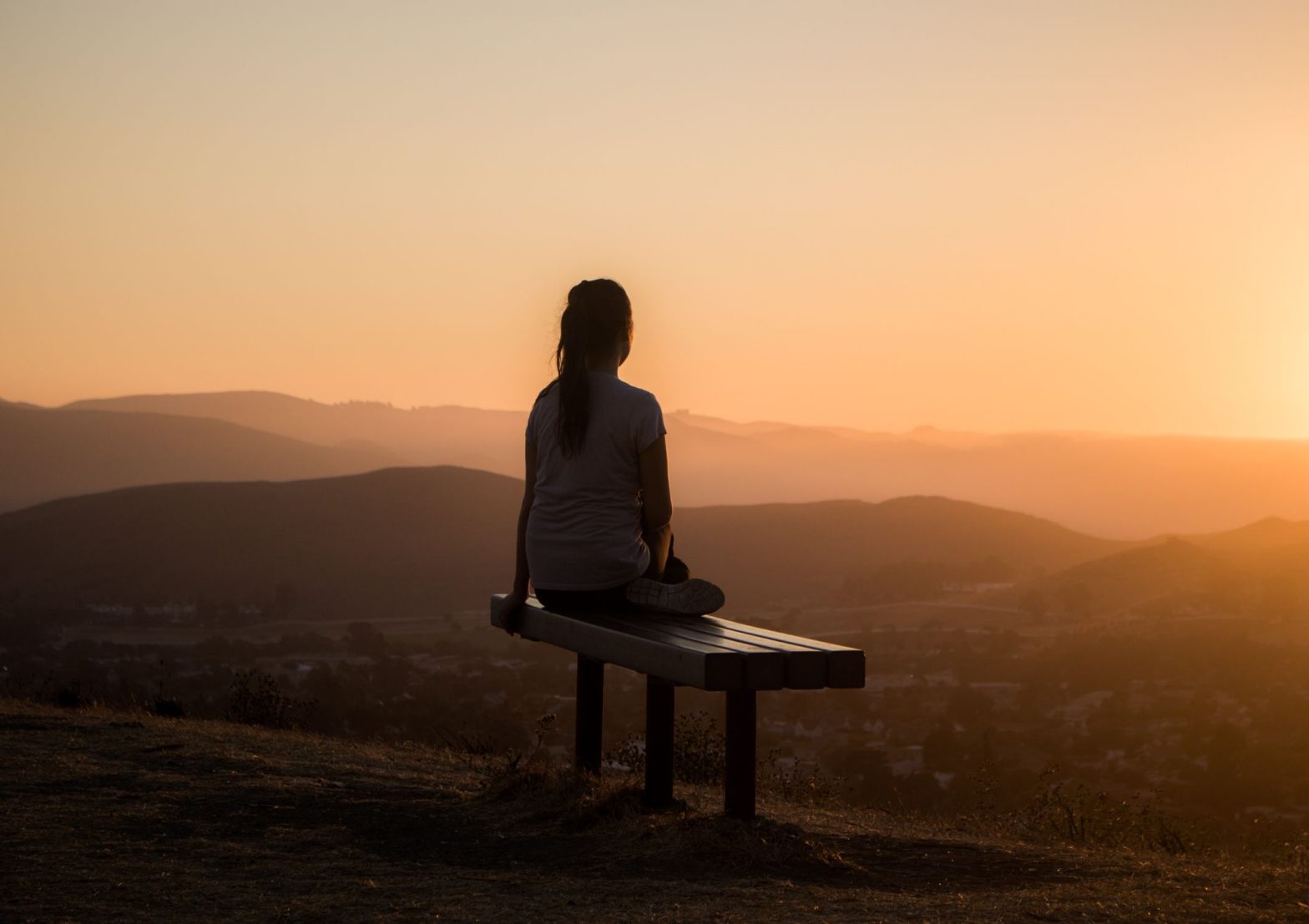 Person sitting on a bench at sunset looking calm and relaxed, sitting mindfully and taking care of their mental health and wellbeing