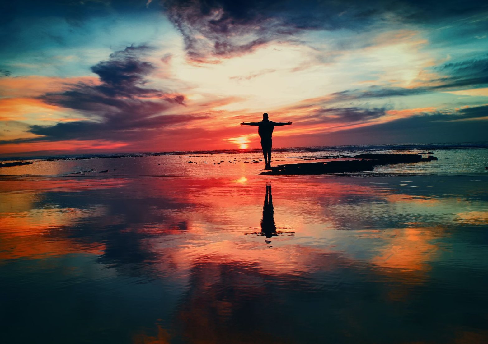 Person standing as a silhouette with arms open wide amid beautiful sunset looking content and joyful