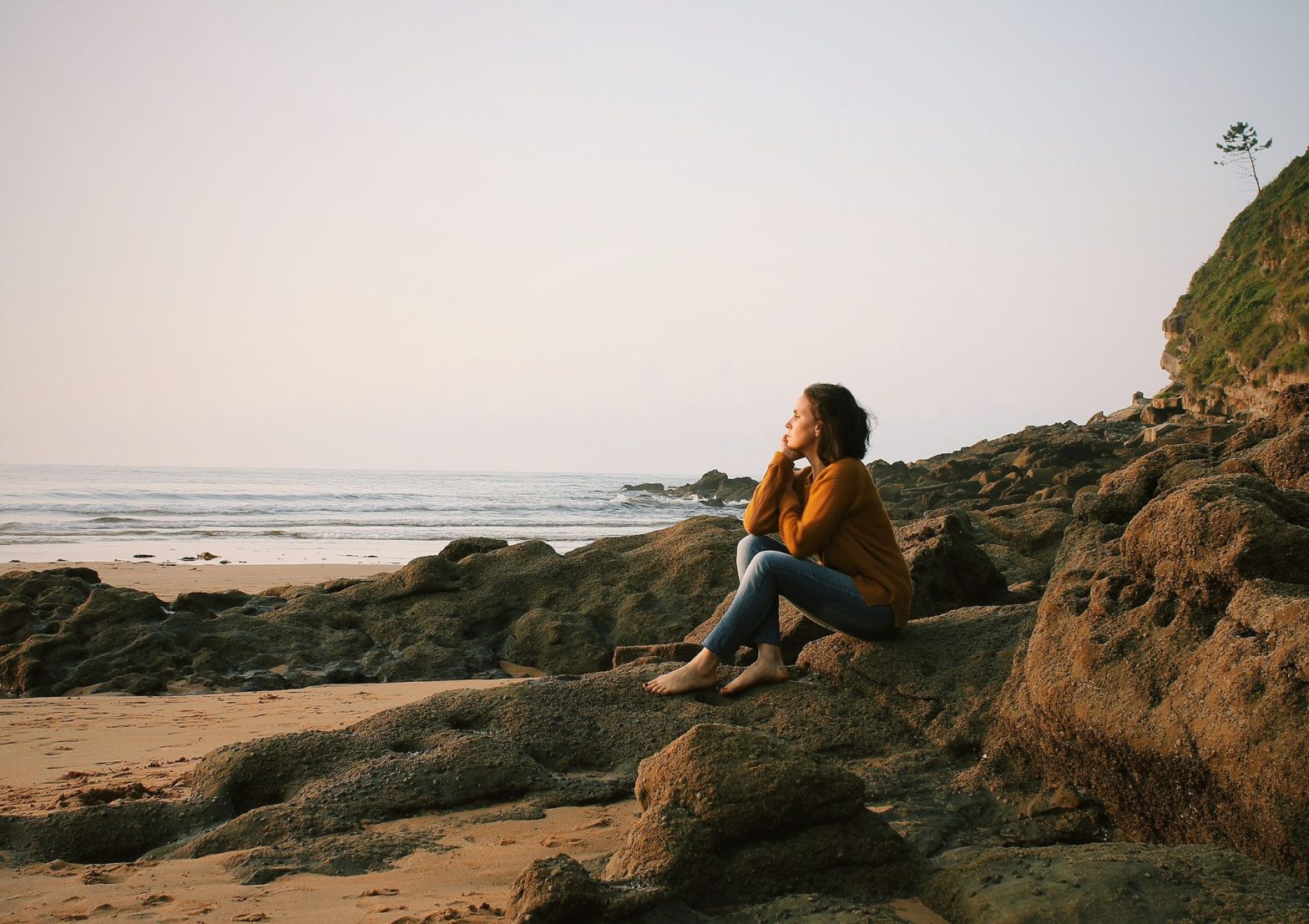 Image shows someone sitting deep in thought on the rocks, being still and mindful in the fresh air for the benefit of their mental health and wellbeing