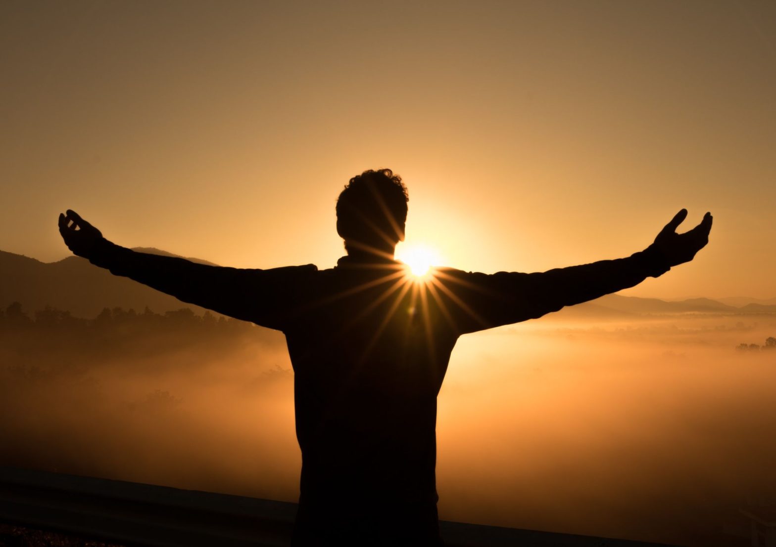 Person standing with their arms out wide mindfully soaking in the moment for the good of their mental health and wellbeing, during a beautiful sunrise