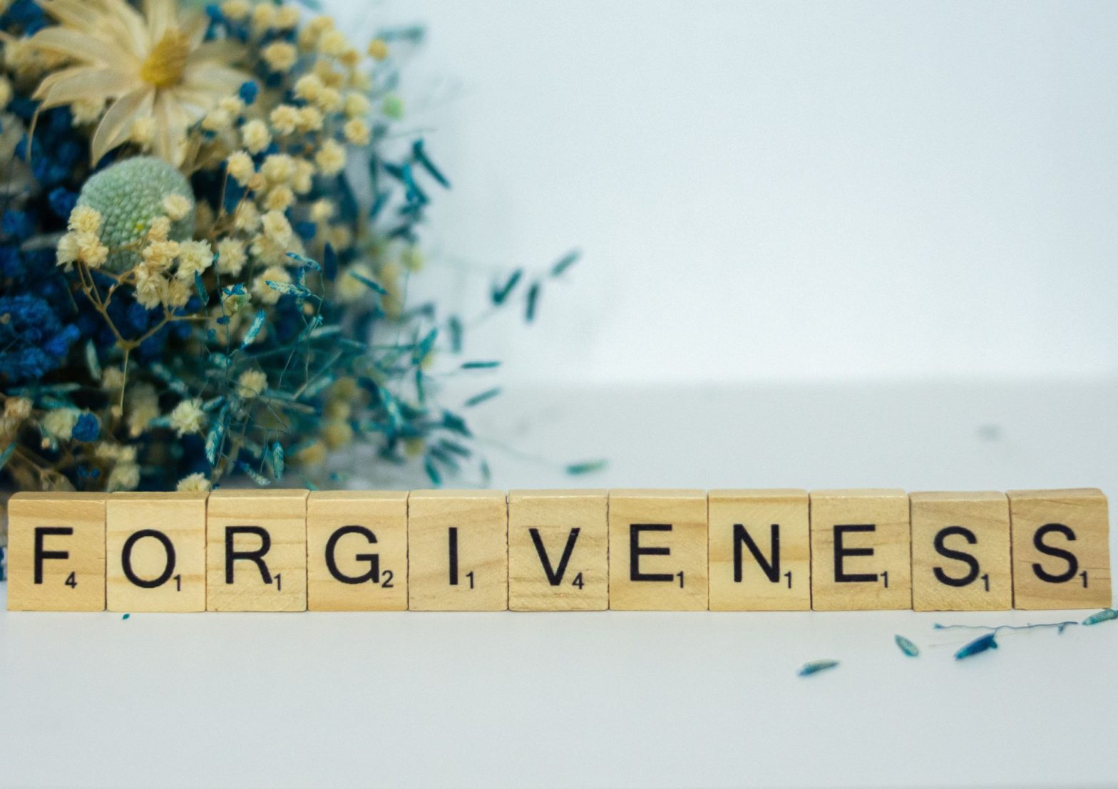 Image shows scrabble letter all lined up spelling the word forgiveness, with a bunch of flowers in the background