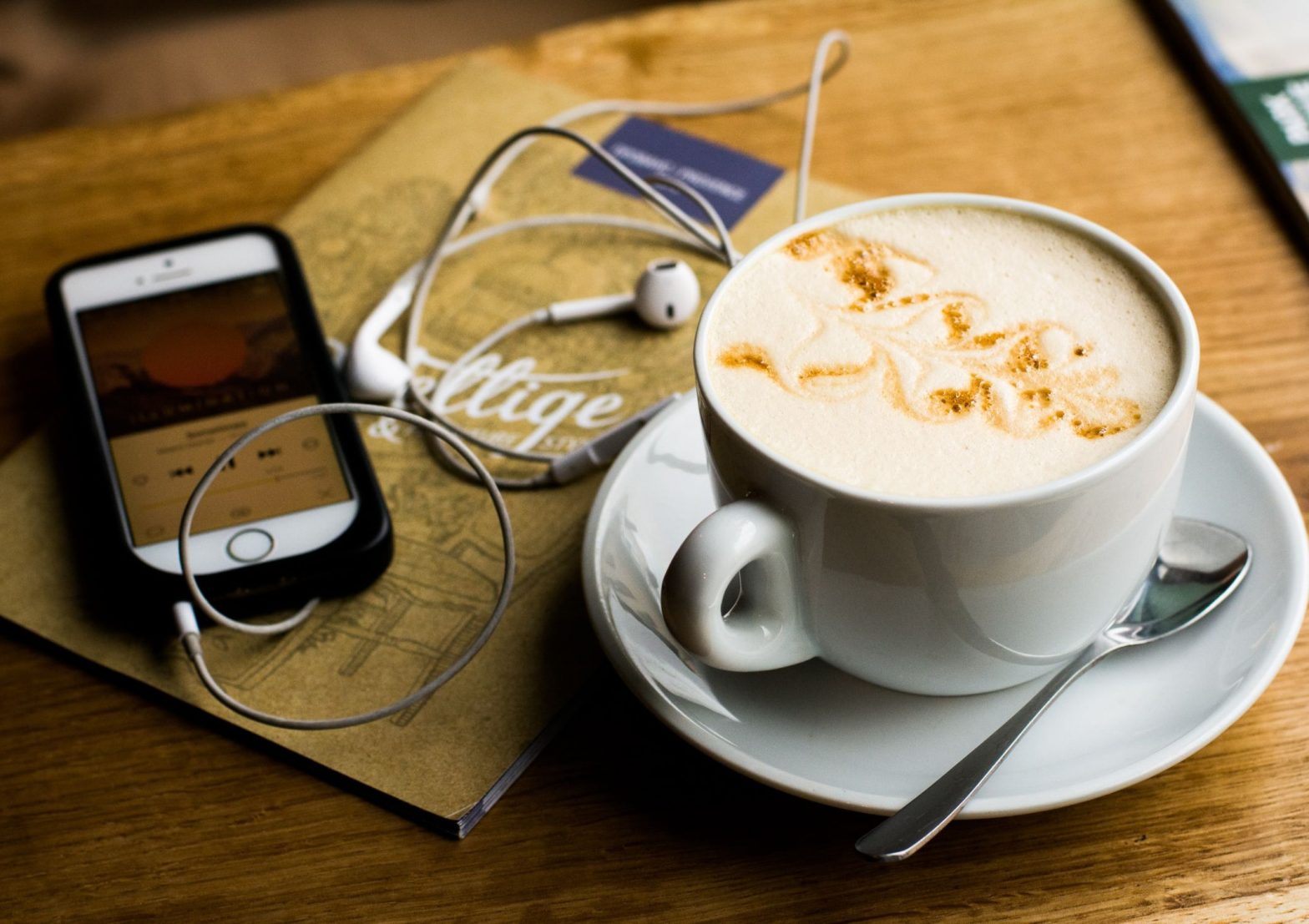 Image shows a fresh cup of coffee beside a mobile phone and ear-phones