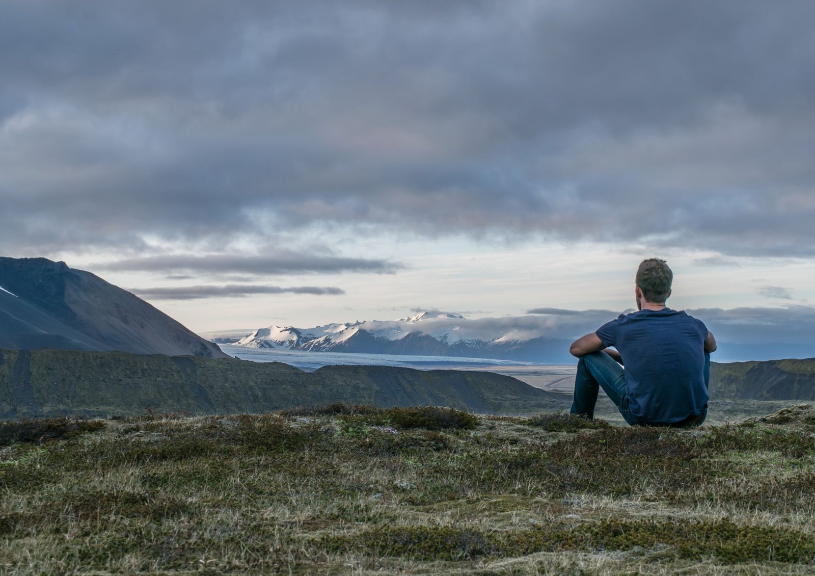 Image shows a person sitting in the countryside looking into the distance in an act of self-reflection and contemplation