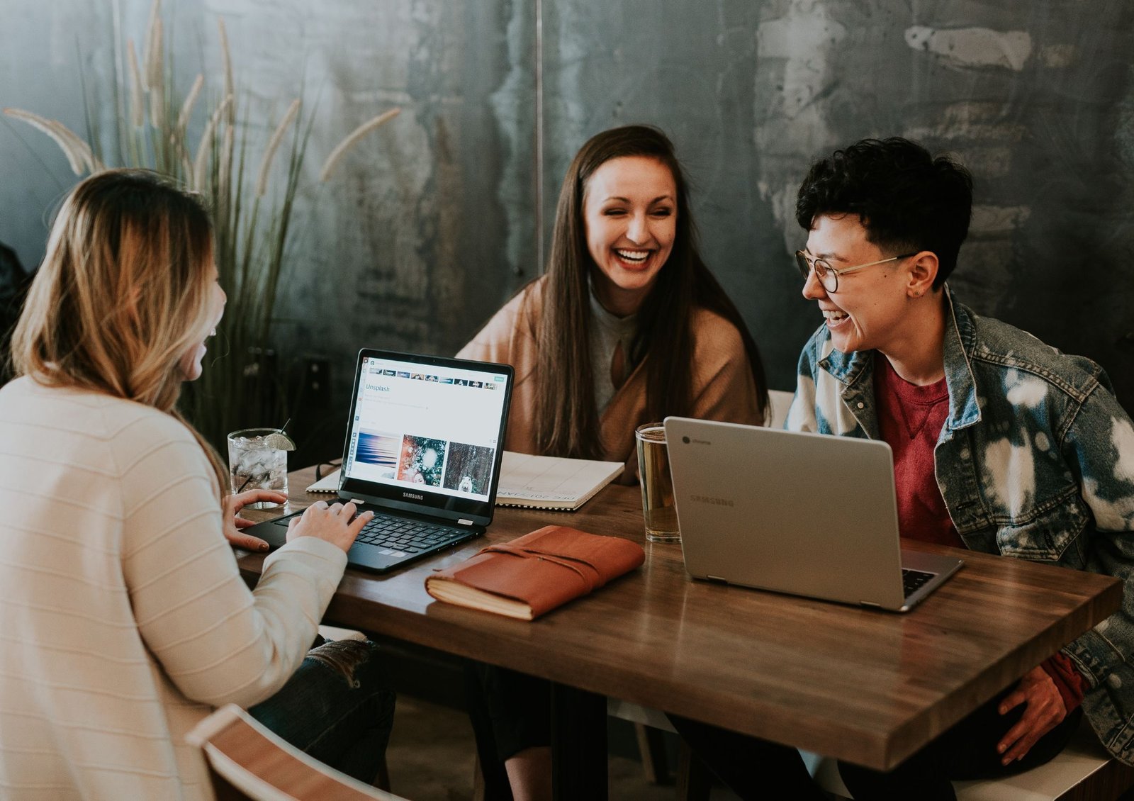 Image shows three colleagues working together at a table with their laptops looking relaxed and happy