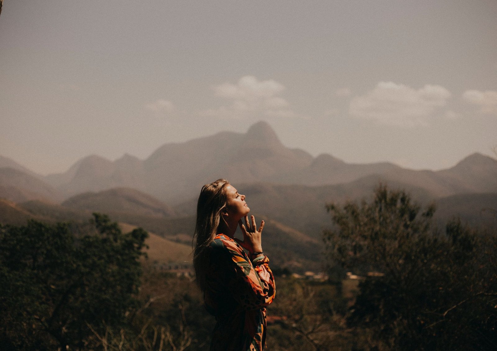 Image shows a person in the countryside, with mountains in the background, deep in thought and basking in the sunlight