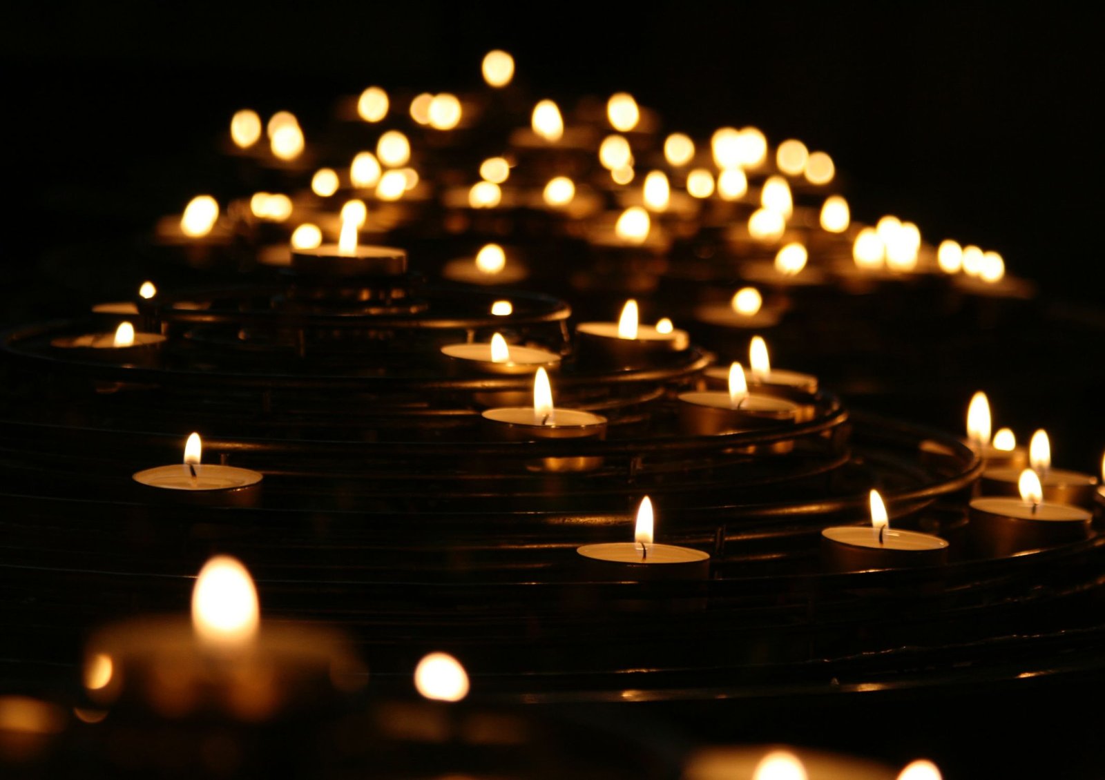 Image shows a series of lit candles with their flames glowing in the dark like a symbol of hope, memories and compassion during times of grief