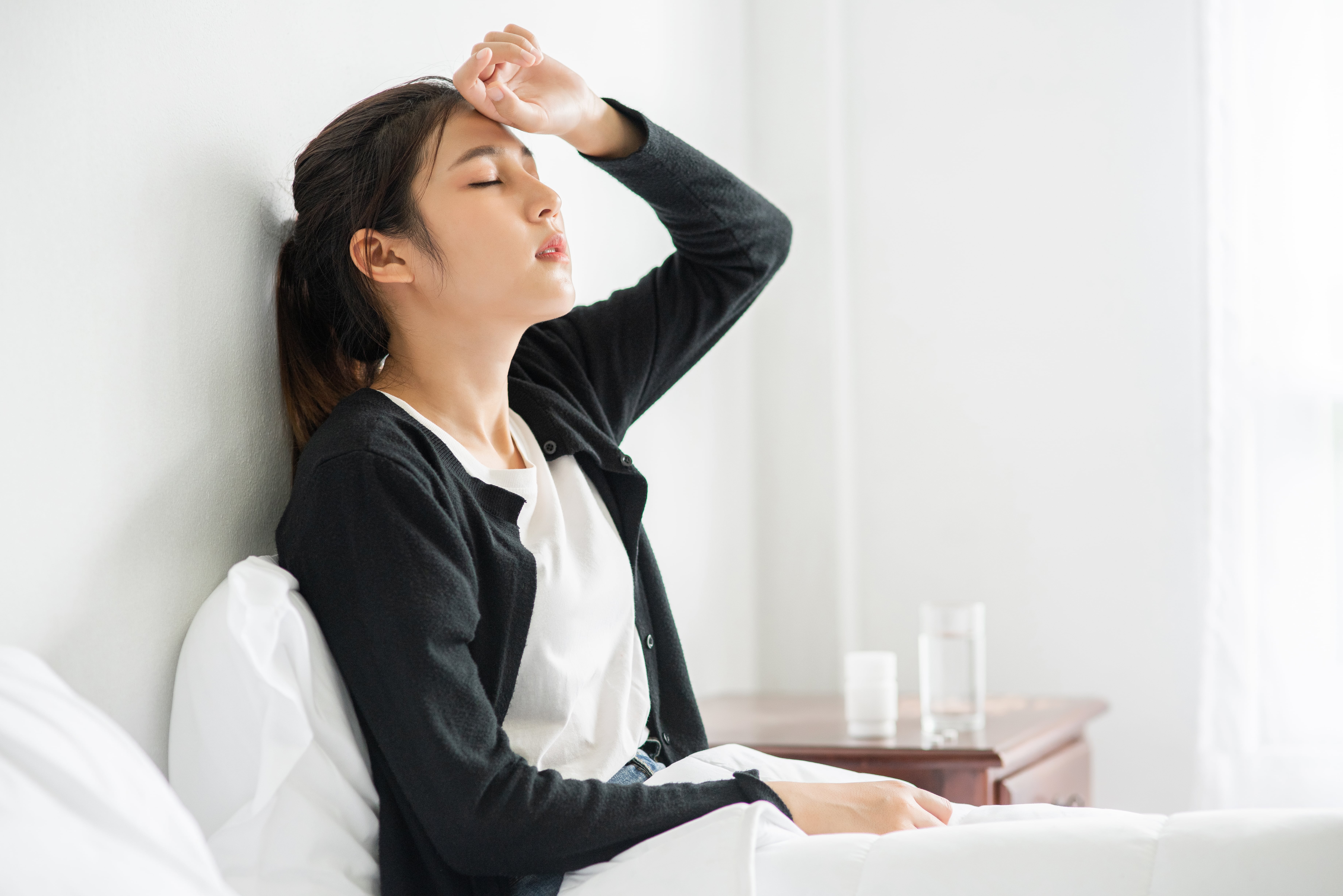 uncomfortable woman sits bed has medicine table min